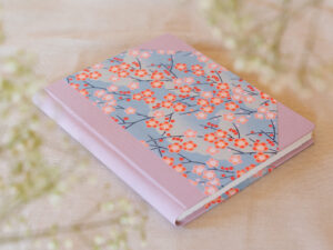 notes w kropki, bullet journal w kwiaty leży na jasnym stole. Okładkę zdobią kwiaty i jasne pastelowe płótno